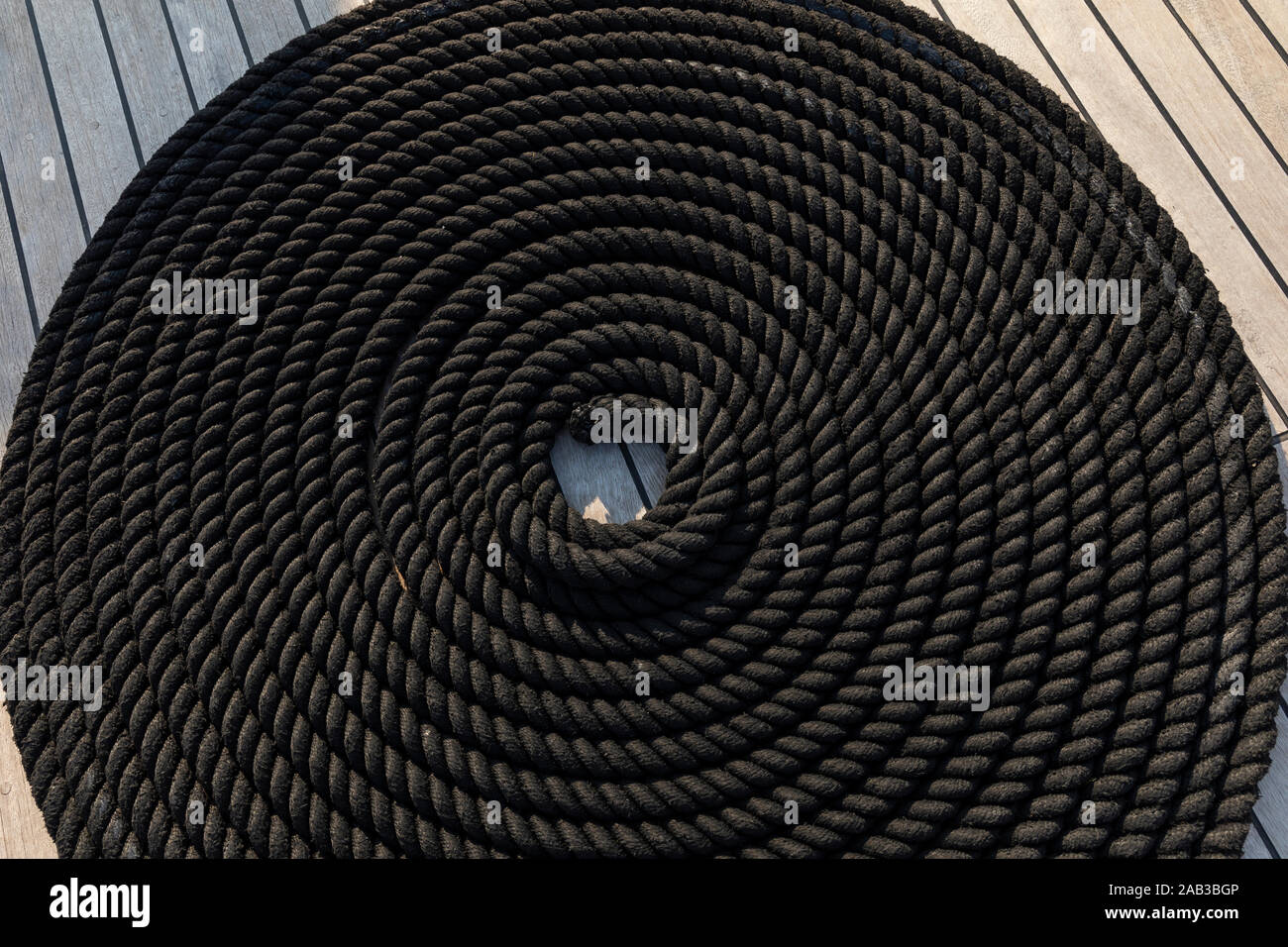 Corda nera nella forma di una bobina a bordo di una barca posa sul ponte. Realizzato in un bellissimo anello tradizionale twist per fissare la corda e la creazione di Foto Stock