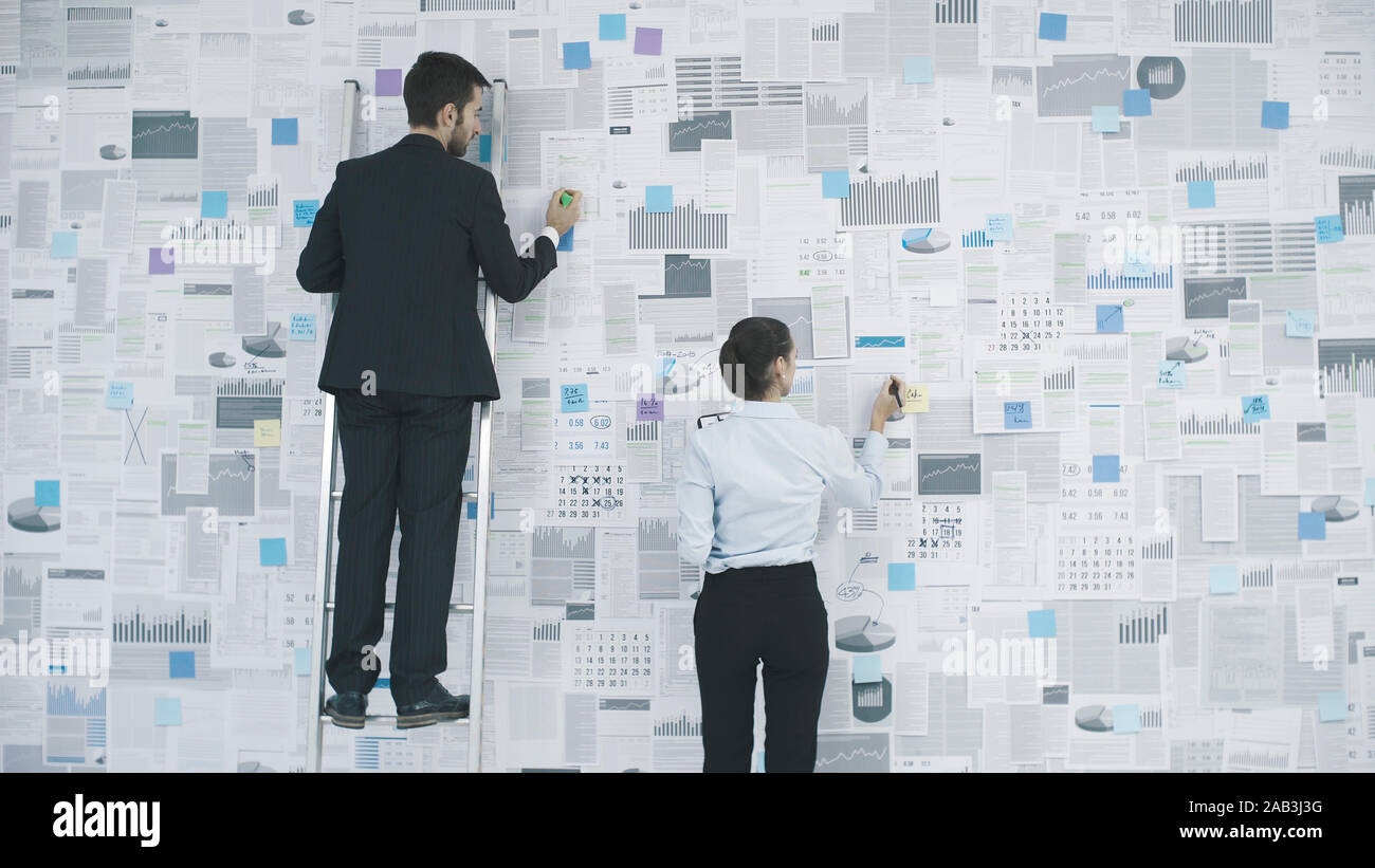 Dirigenti aziendali della pianificazione della loro strategia di business: stanno analizzando molti resoconti finanziari e grafici appeso a una parete Foto Stock