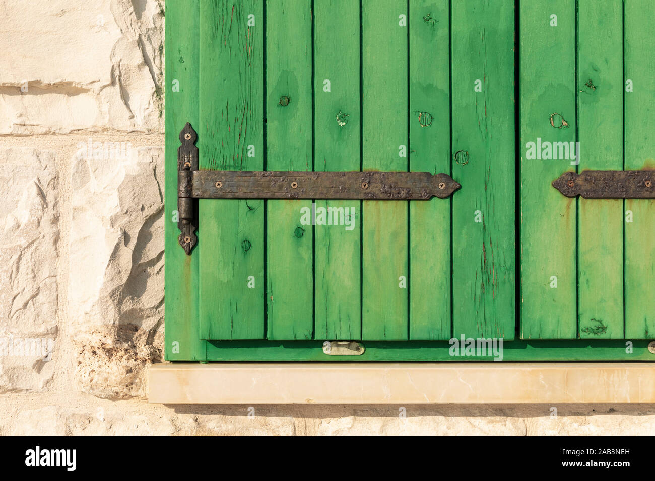 Chiudere fino all'esterno del dipinto di verde chiuso fienile in legno ciechi della finestra con i dettagli in metallo e la luce colorata parete calcarea con grande torta di pietra Foto Stock