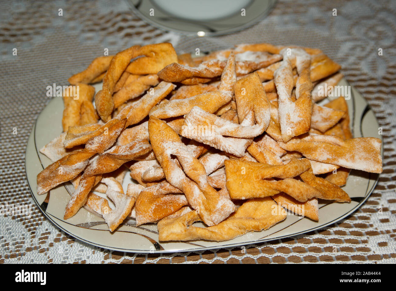 L'impasto dolce fritto si stacca con zucchero a velo su un tavolo con tovaglia in pizzo bianco Foto Stock