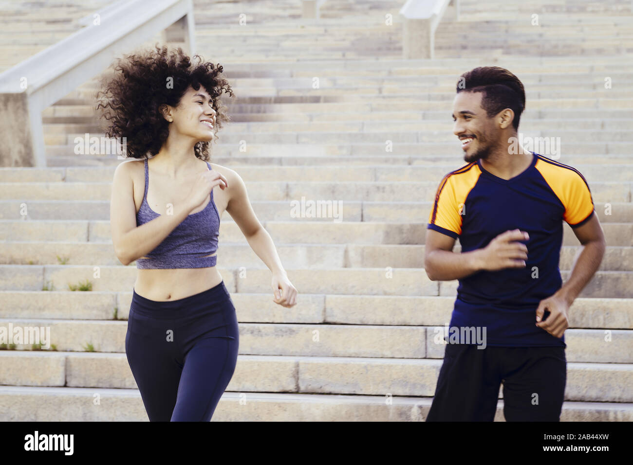 Donna sorridente e uomo felice in esecuzione al piano di sotto sulla città di scale, fitness, urban allenamento sportivo e di uno stile di vita sano concetto Foto Stock