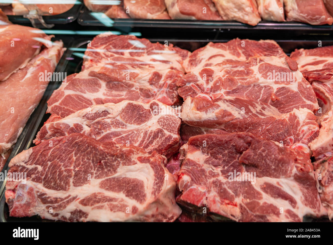 Selezione di carni di qualità presso un negozio di macellaio, macellato il maiale in un espositore refrigerato sotto vetro, vicino. Foto Stock