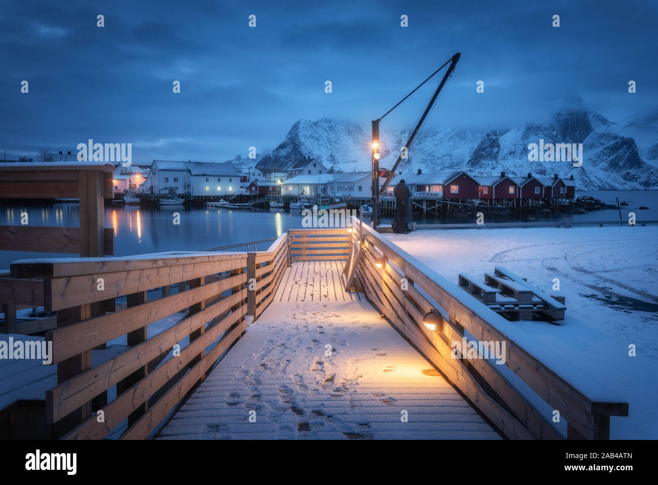 Snowy molo in legno sulla costa del mare con luci, case e barche Foto Stock