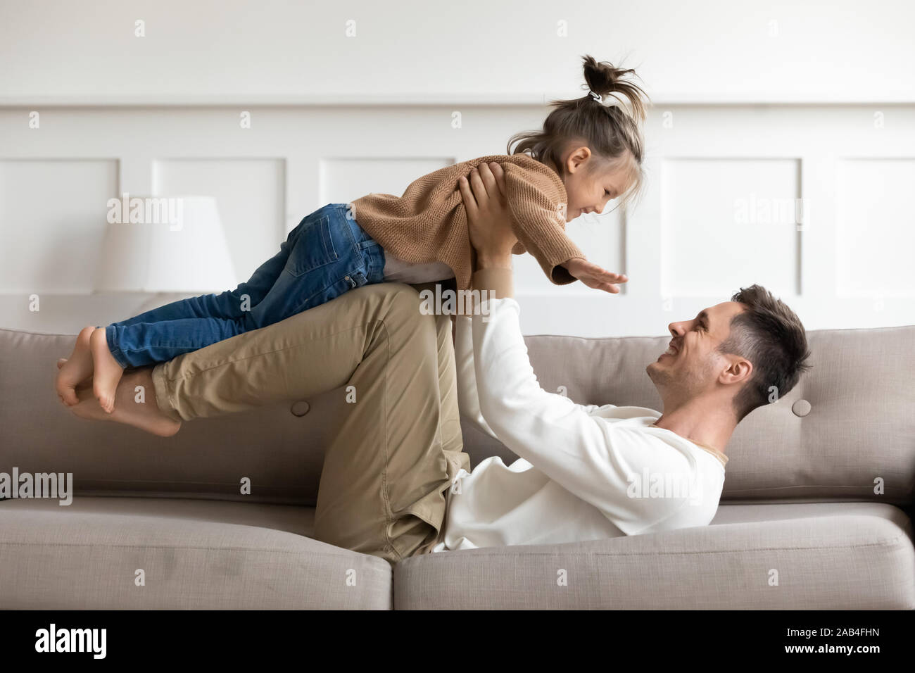 Padre Felice il sollevamento carino kid figlia fino a giocare sul divano Foto Stock