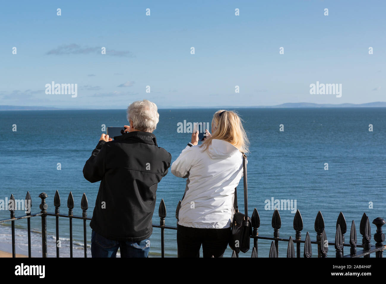 Senior / medio-età coppia in vacanza in riva al mare a scattare foto di vista su telefoni cellulari Foto Stock