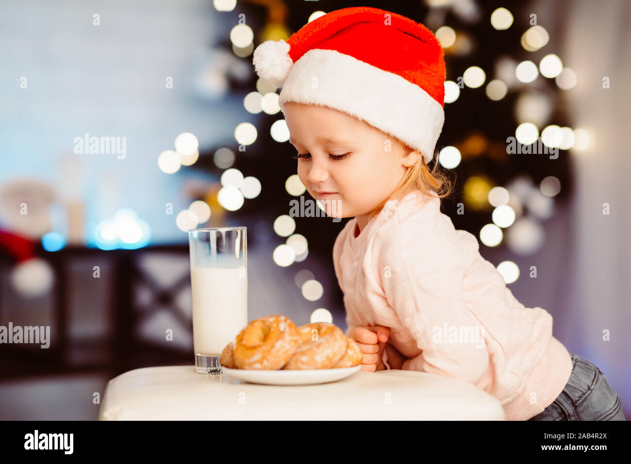 Carino bambina guardando tratta per Santa nei pressi di albero di Natale Foto Stock