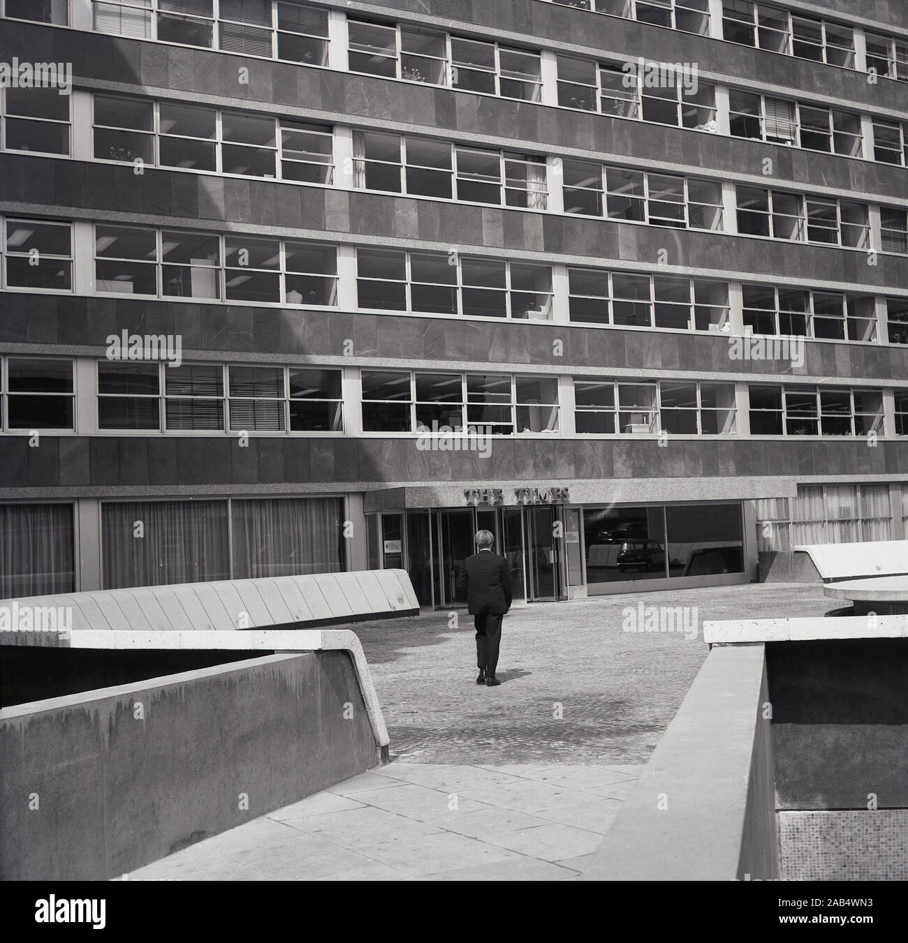 Anni sessanta, historcial, uomo su un piazzale a camminare verso un moderno costruito in cemento ufficio edificio d'epoca, casa del quotidiano britannico "tempi", Londra, Inghilterra, Regno Unito. Foto Stock