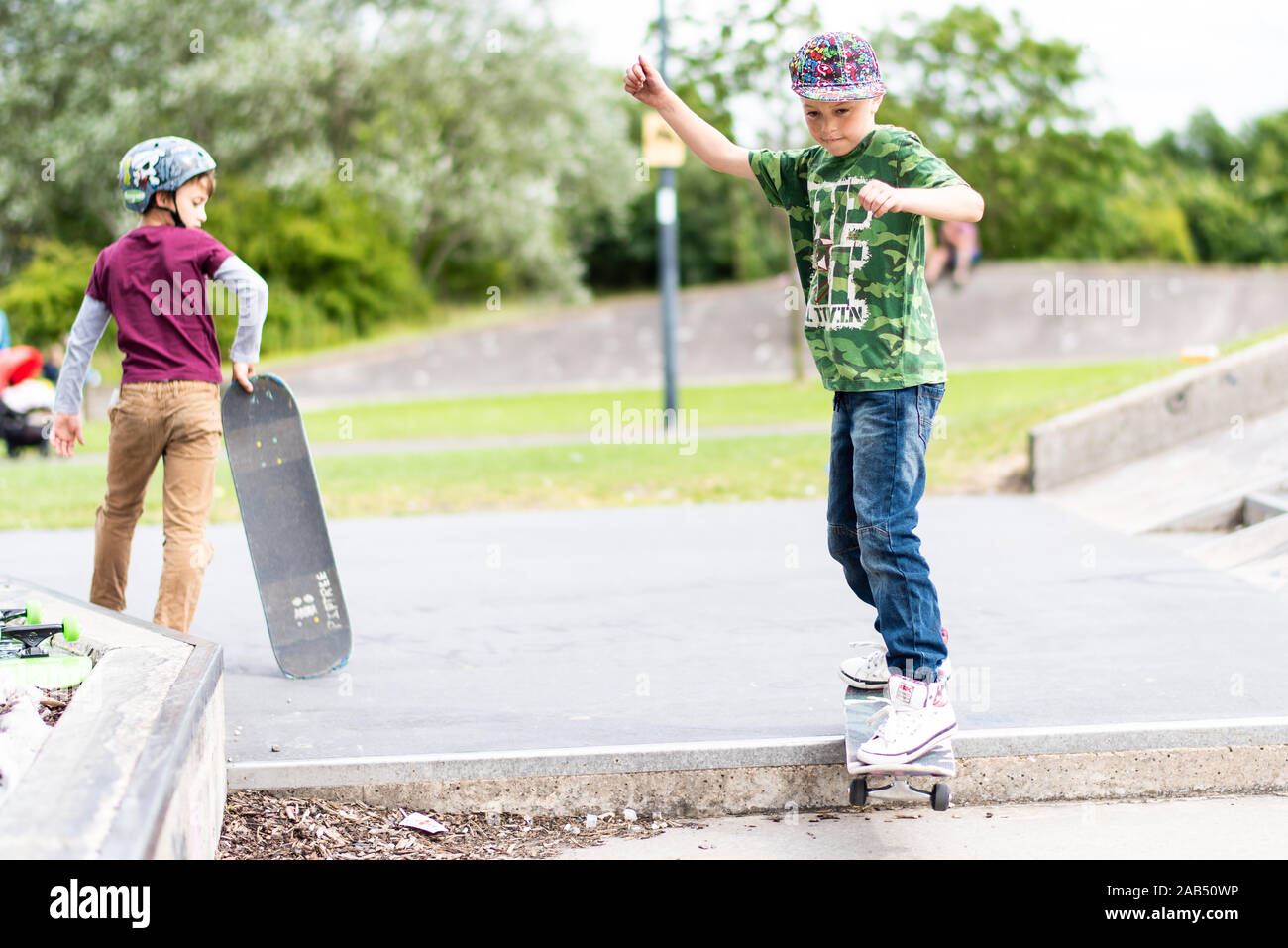 Un ragazzino con ADHD, autismo, sindrome di Asperger pratica scendendo alcuni scalini presso il locale skatepark con il suo istruttore di skateboard guardando su Foto Stock