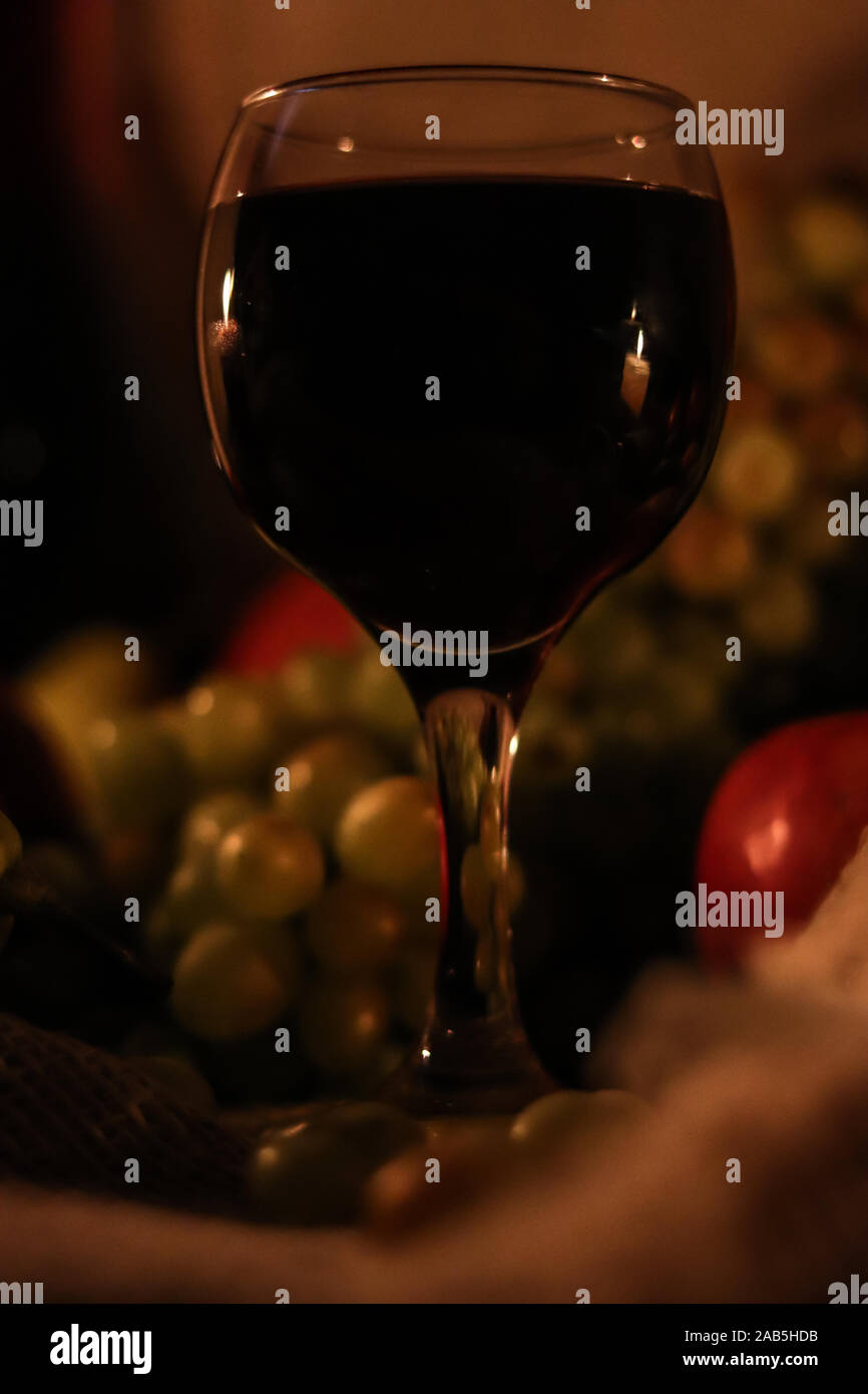 Bicchiere di vino rosso con la riflessione di due fiammelle delle candele su di esso da vicino e frutti: uva, Apple su un letto di sacco sullo sfondo Foto Stock