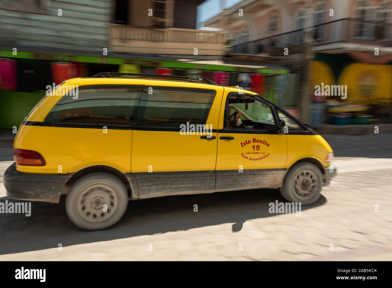 L' immagine di un taxi giallo van guidando lungo la strada di ciottoli in San Pedro su Ambergris Caye nel Belize. Una immagine viene eseguita utilizzando una tecnica di panning ma Foto Stock