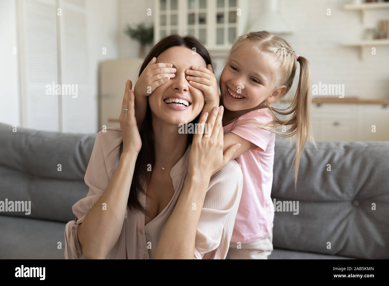 Carino kid figlia chiudendo gli occhi di felice mamma rendendo sorpresa Foto Stock