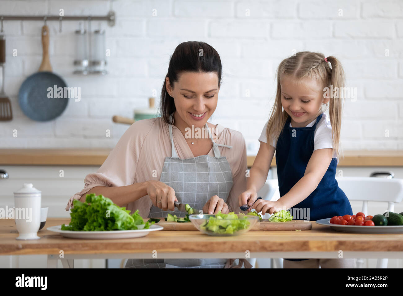 Carino kid figlia aiutando la mamma il taglio di insalata fresca in cucina Foto Stock
