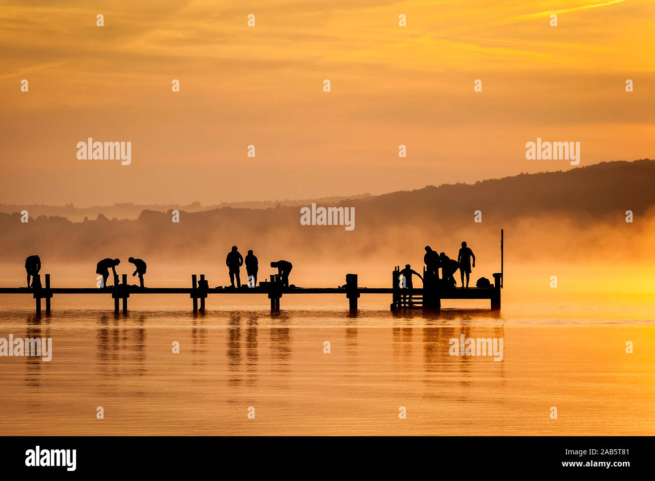 Viele Menschen, die im Morgengrauen Sport aufeinem Bootssteg am Starnberger See machen Foto Stock