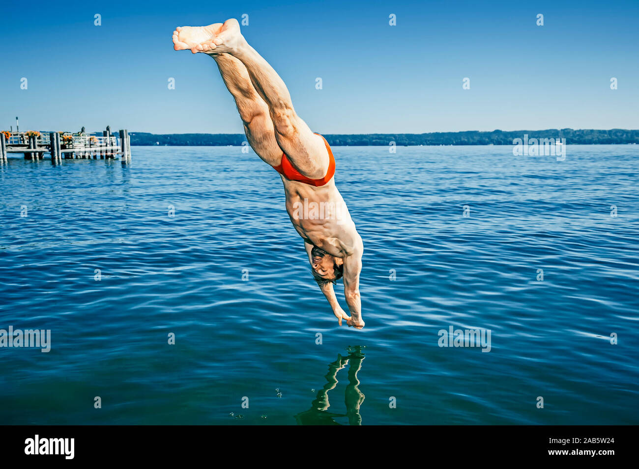 Ein junger Mann in roter Badehose, der in den Starnberger See springt Foto Stock