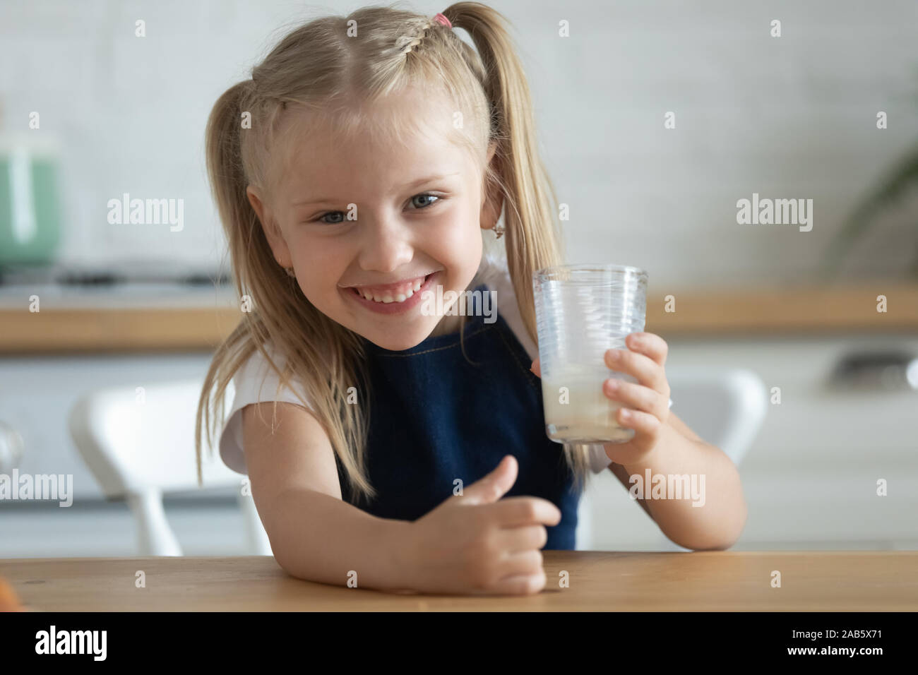 Funny happy carina ragazza di capretto tenere il vetro bere latte fresco Foto Stock