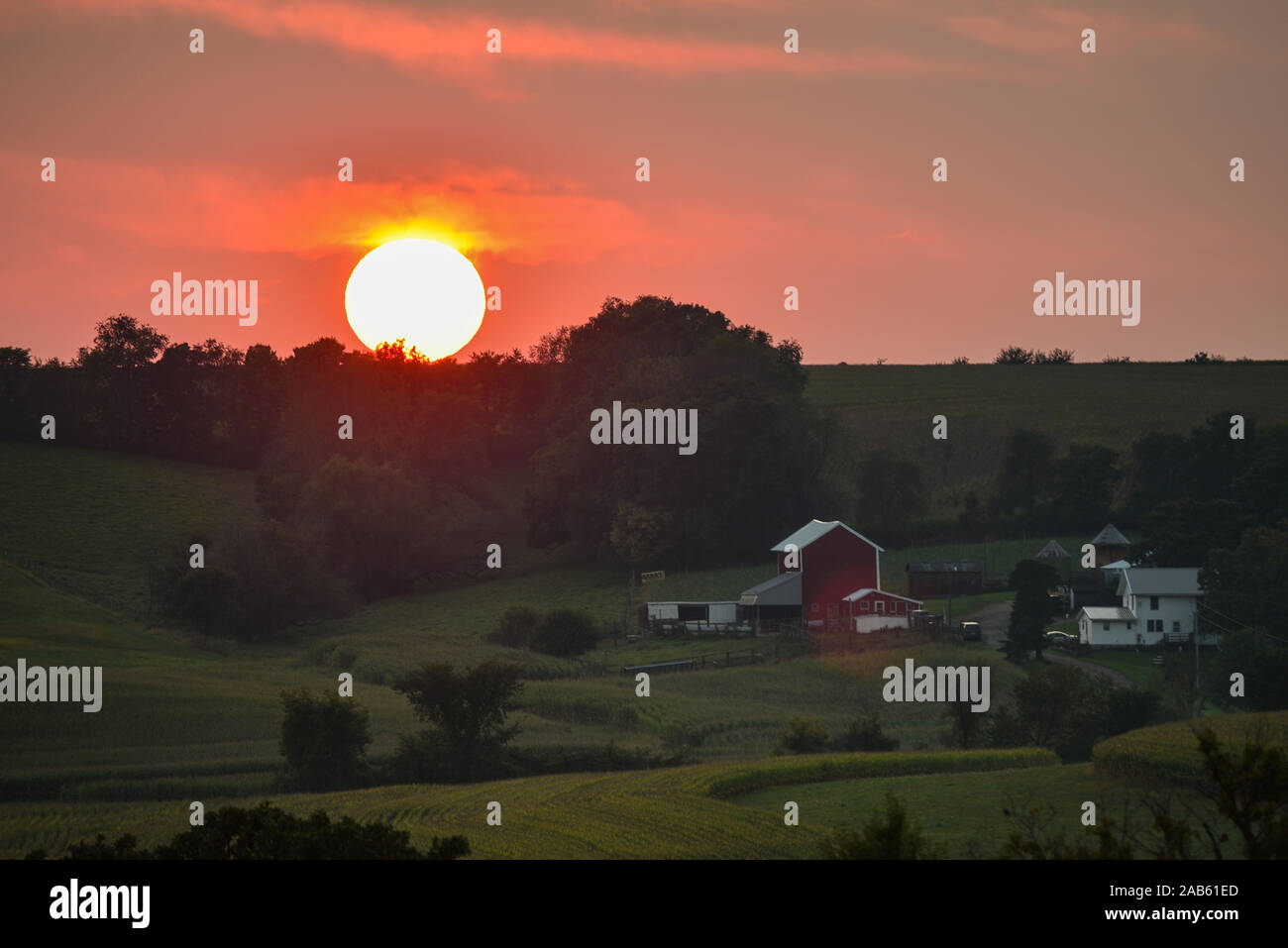 Arancio brillante tramonto sul crinale distante, bosco in superfici agricole fiorenti comunità, con la fattoria, granai e raccolti in campi, Browntown, Wisconsin, STATI UNITI D'AMERICA Foto Stock