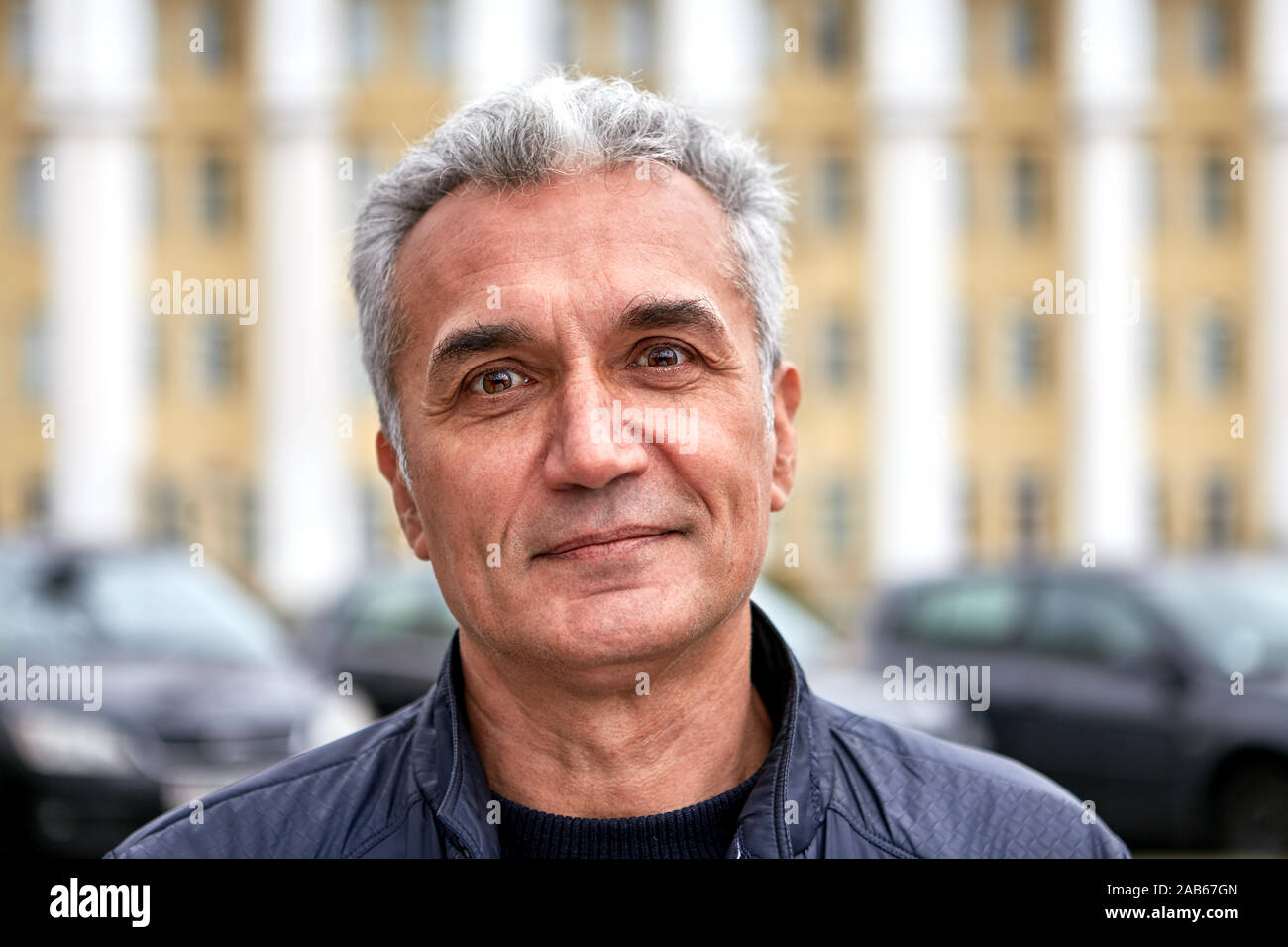 Ritratto di una matura bello gentile uomo con corti capelli color argento all'esterno. Età allegro dentista è in piedi sulla strada e in posa. Felice senior pe Foto Stock