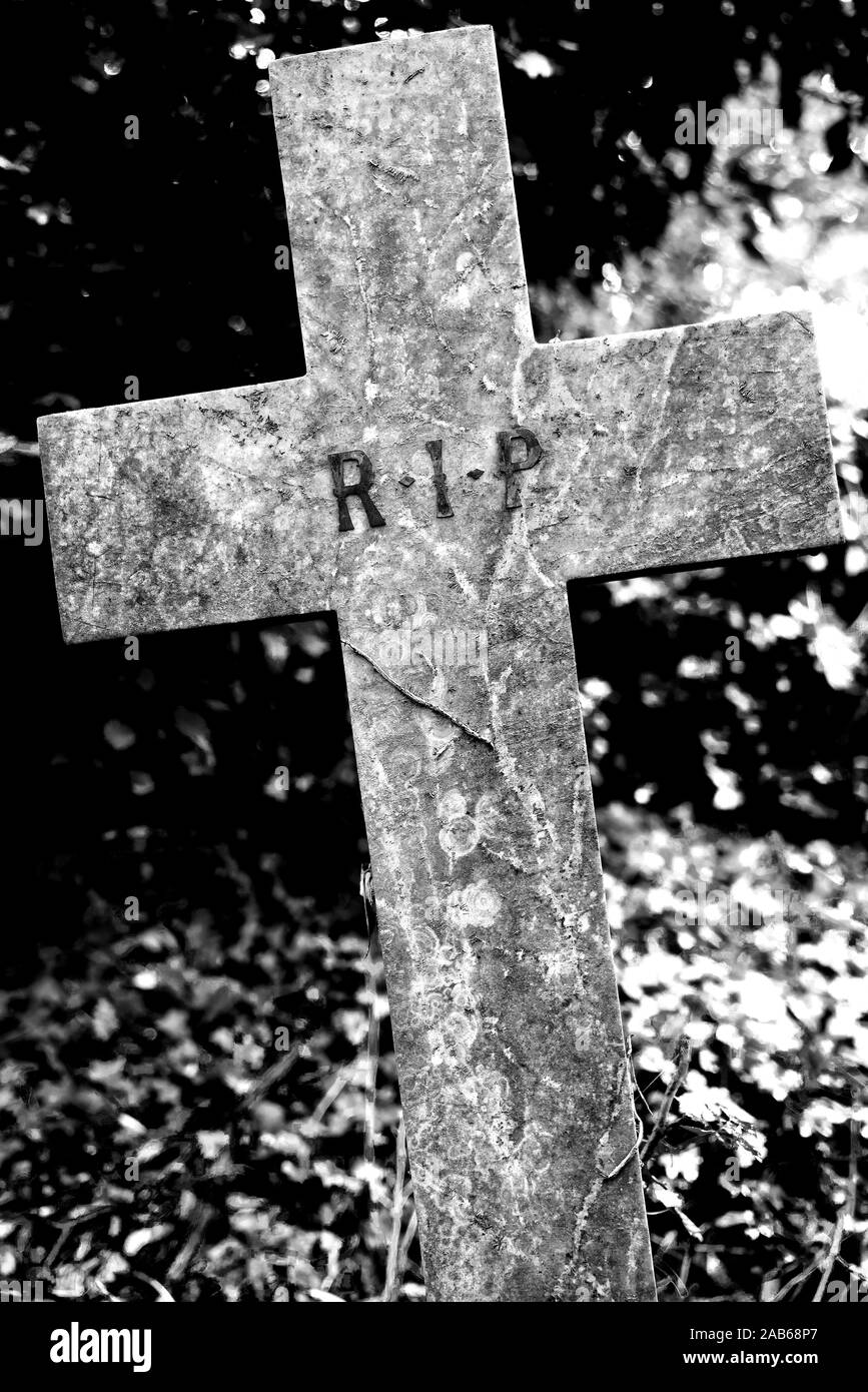 Un wonky croce di pietra in un cimitero con R.I.P segno inciso Foto Stock