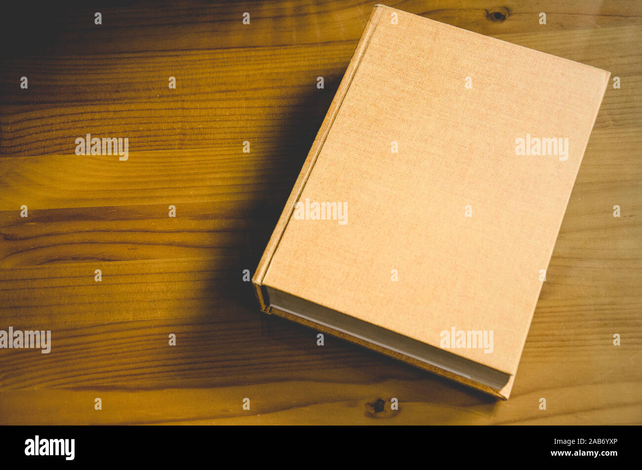 Libro con copertina vuota in cui è possibile inserire un testo o un disegno, appoggiato su un tavolo di legno con spazio negativo sul lato sinistro Foto Stock