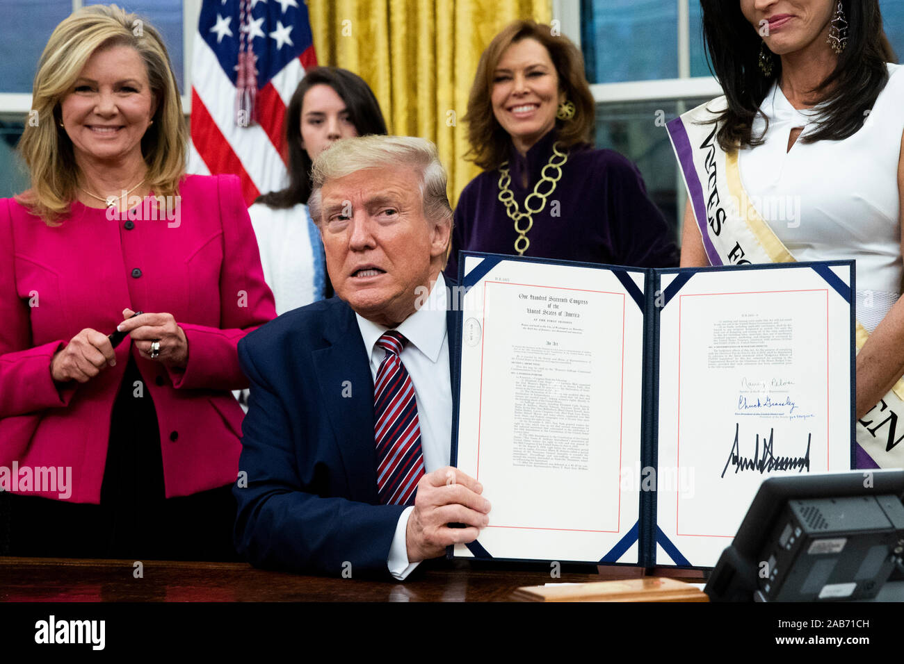 Il presidente statunitense Trump (C) contiene fino "il suffragio femminile Centennial una moneta commemorativa atto ", dopo averlo firmato durante una cerimonia, accanto a Stati Uniti il senatore Marsha Blackburn (Repubblicano del Tennessee) (L), nell'Ufficio Ovale della Casa Bianca di Washington, DC, Stati Uniti d'America, 25 novembre 2019. Trump firmato "H.R. 2423, il suffragio femminile Centennial una moneta commemorativa atto " - un disegno di legge dirigere il Tesoro USA alla menta e rilascio fino al quattrocento mila one-dollar monete d'argento per onorare le donne che hanno giocato un ruolo nella raccolta di supporto per il XIX emendamento.Credit: Michael Reynolds/Piscina via CNP /Me Foto Stock