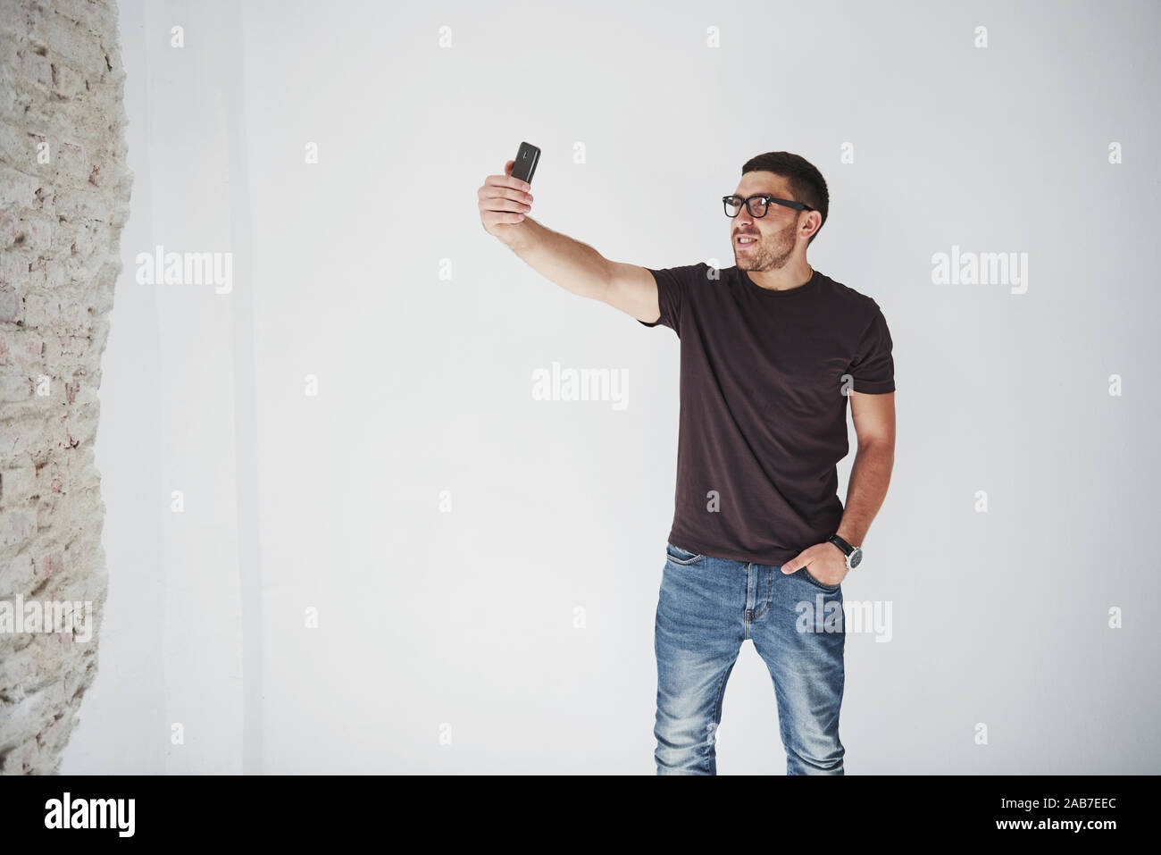 Giocoso uomo barbuto rendendo selfie sullo smartphone e muro bianco sullo sfondo Foto Stock