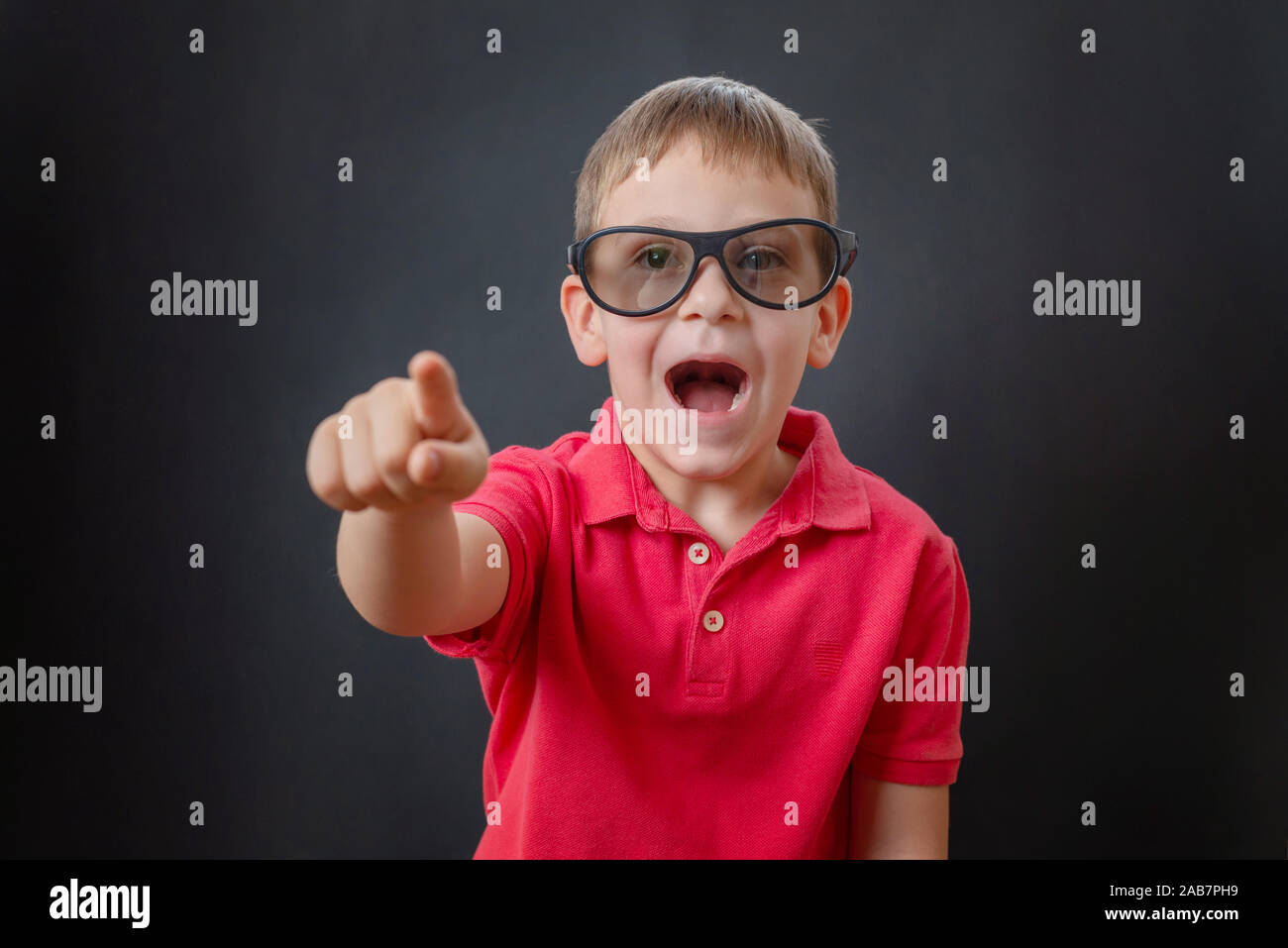 Il ragazzo ride e punta il dito in un momento divertente nel filmato. Indossa gli occhiali 3d sulla sua testa. Sfondo nero. Foto Stock
