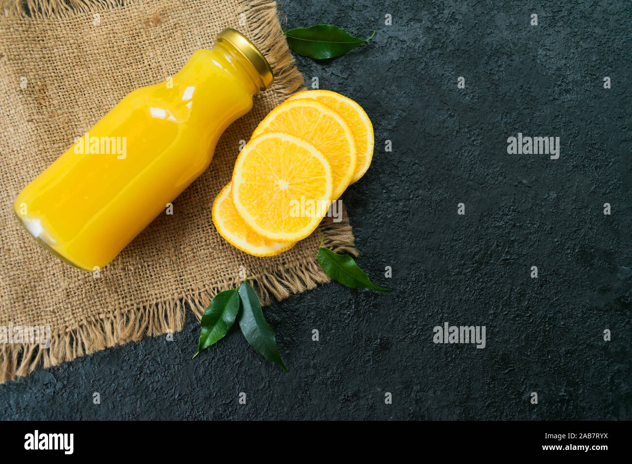 Il succo di arancia in una bottiglia e fette di arancia su uno sfondo nero. Lay piatto. Vitamina bere. Spazio di copia Foto Stock