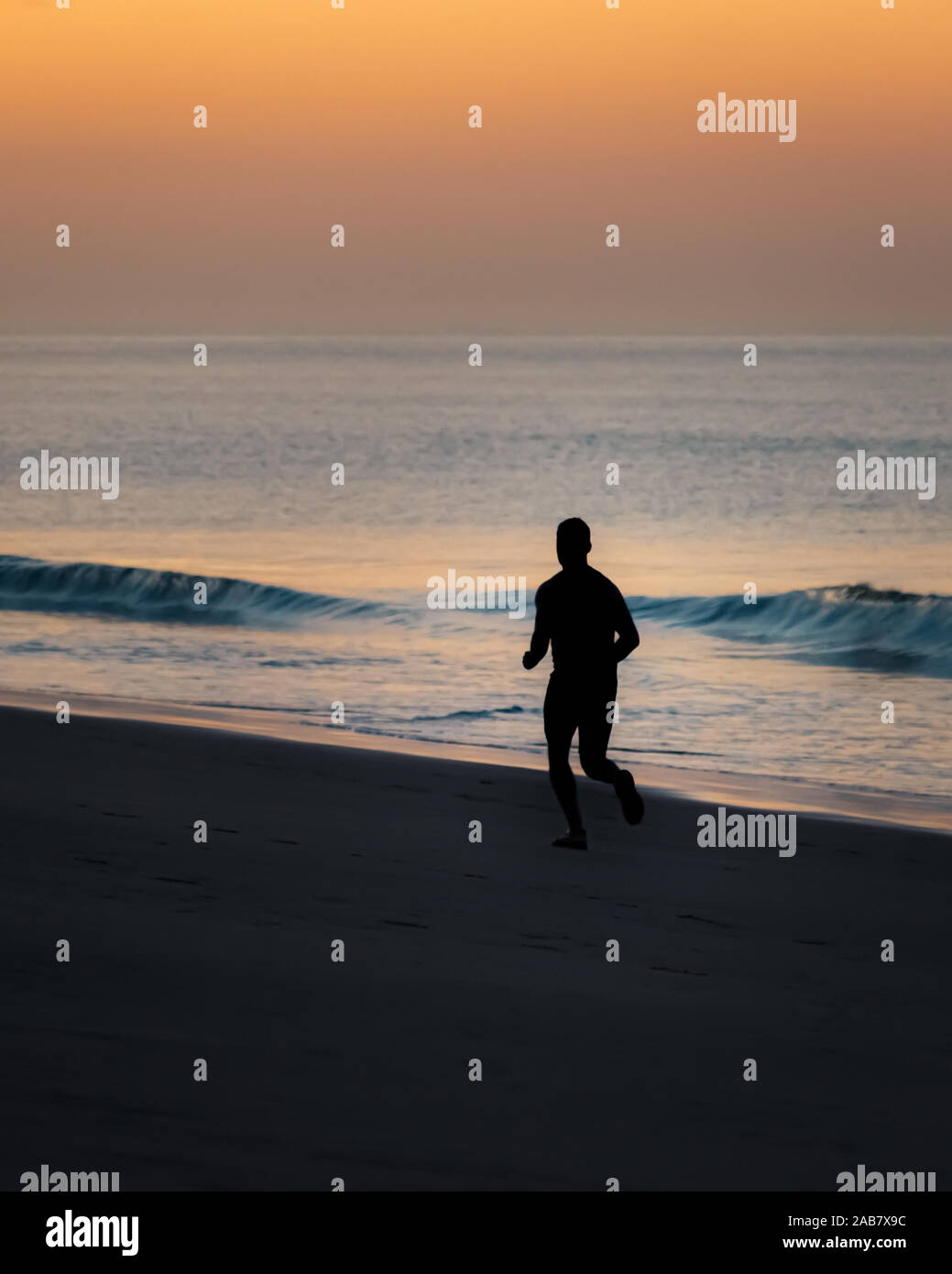 Spiaggia di falesia, Portogallo - 01 Ottobre 2019: Un pareggiatore in silhouette corre lungo la spiaggia di sunrise Foto Stock