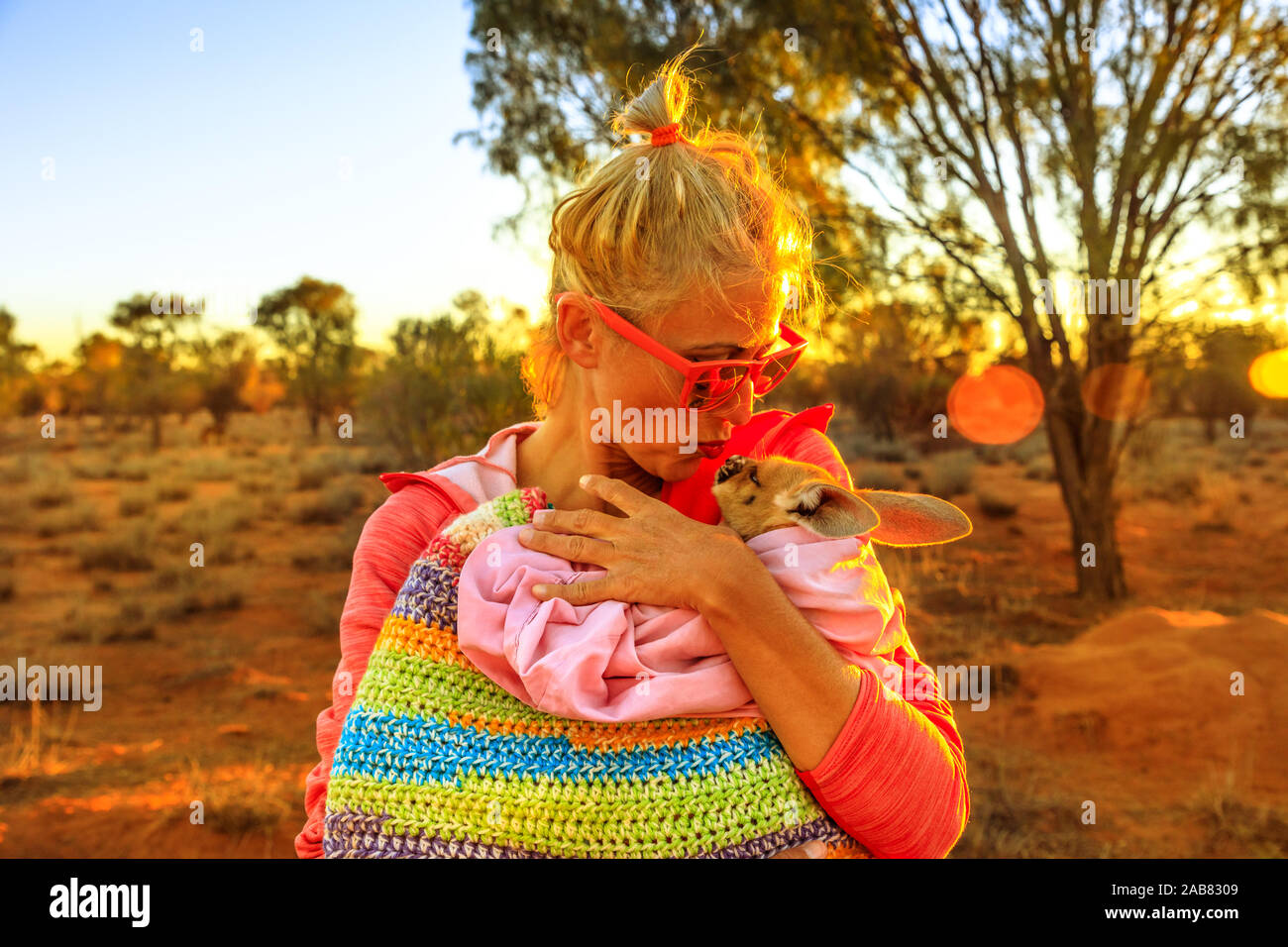 Donna turistica holding e baciare kangaroo joey alla luce del tramonto in Australian Outback Red Centre, Territorio del Nord, l'Australia, il Pacifico Foto Stock