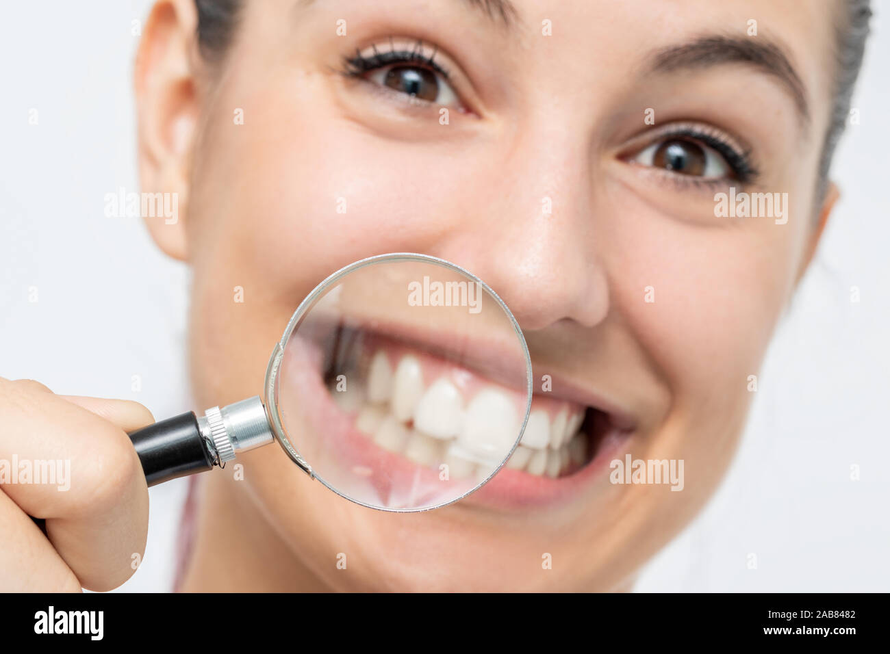 Close up divertente Ritratto di giovane ragazza che mostra denti con lente di ingrandimento. Isolato su sfondo bianco. Foto Stock