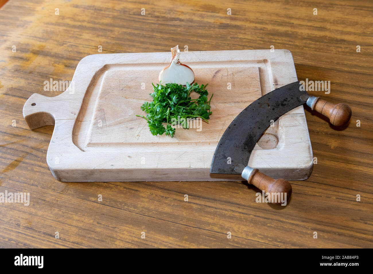 La cipolla, il prezzemolo e il trinciapaglia su una tavola di legno in una cucina Foto Stock