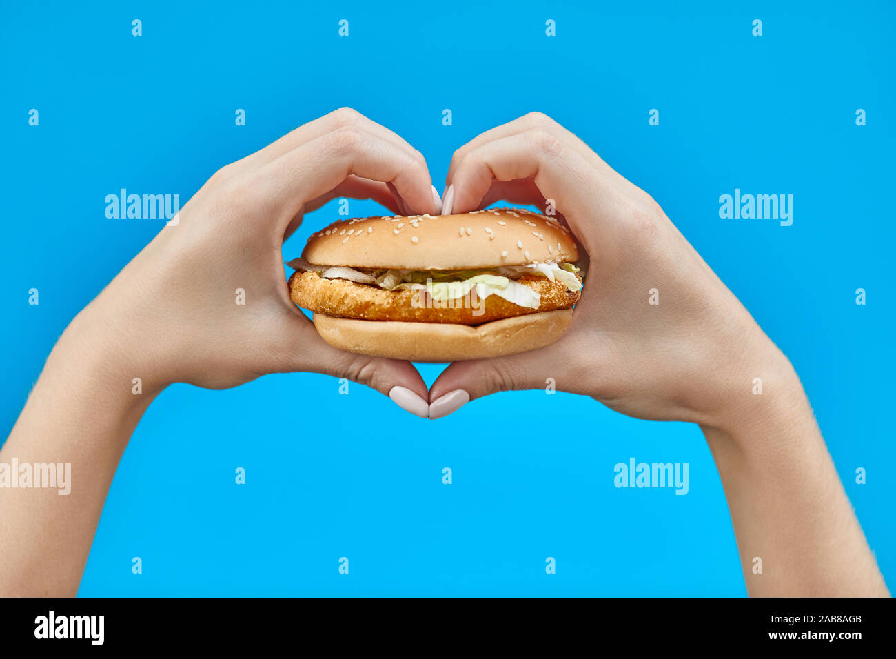 Donna mani tenendo un burger su uno sfondo blu. Due mani facendo segno di cuore con hamburger Foto Stock