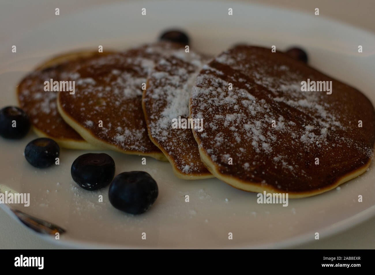 Quattro frittelle spolverato con zucchero a velo e mirtilli sul lato Foto Stock