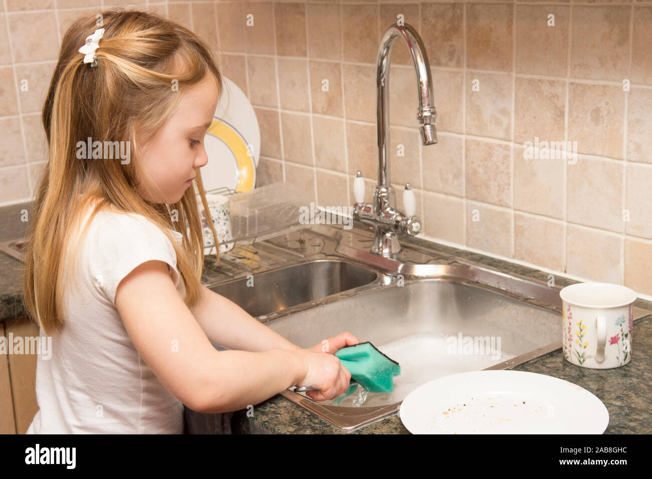 Un giovane bambino lavaggio fino al lavello da cucina, faccende di casa Foto Stock