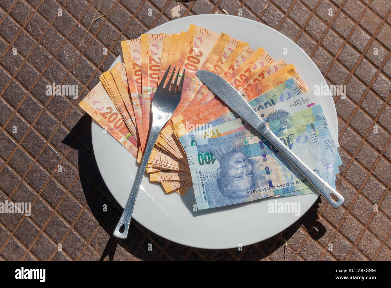 Una vista ravvicinata di uno e due cento Rand note su una piastra con un coltello e forchetta oltre a mostrare la vaule e il prezzo dei generi alimentari Foto Stock