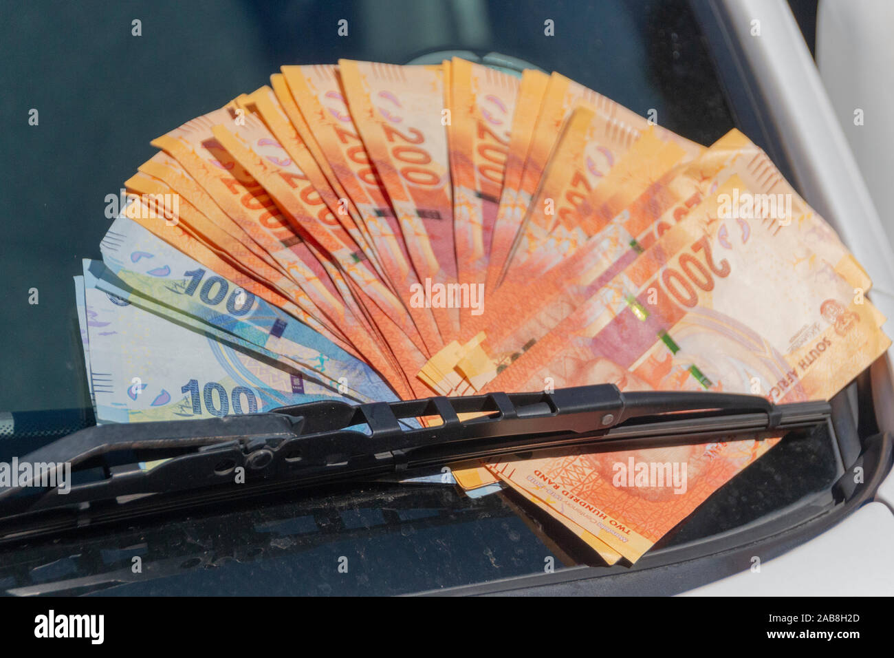 Una vista ravvicinata di uno e due cento rand note sotto un tergicristallo sindscreen per mostrare il costo di parti di automobili Auto ans Foto Stock