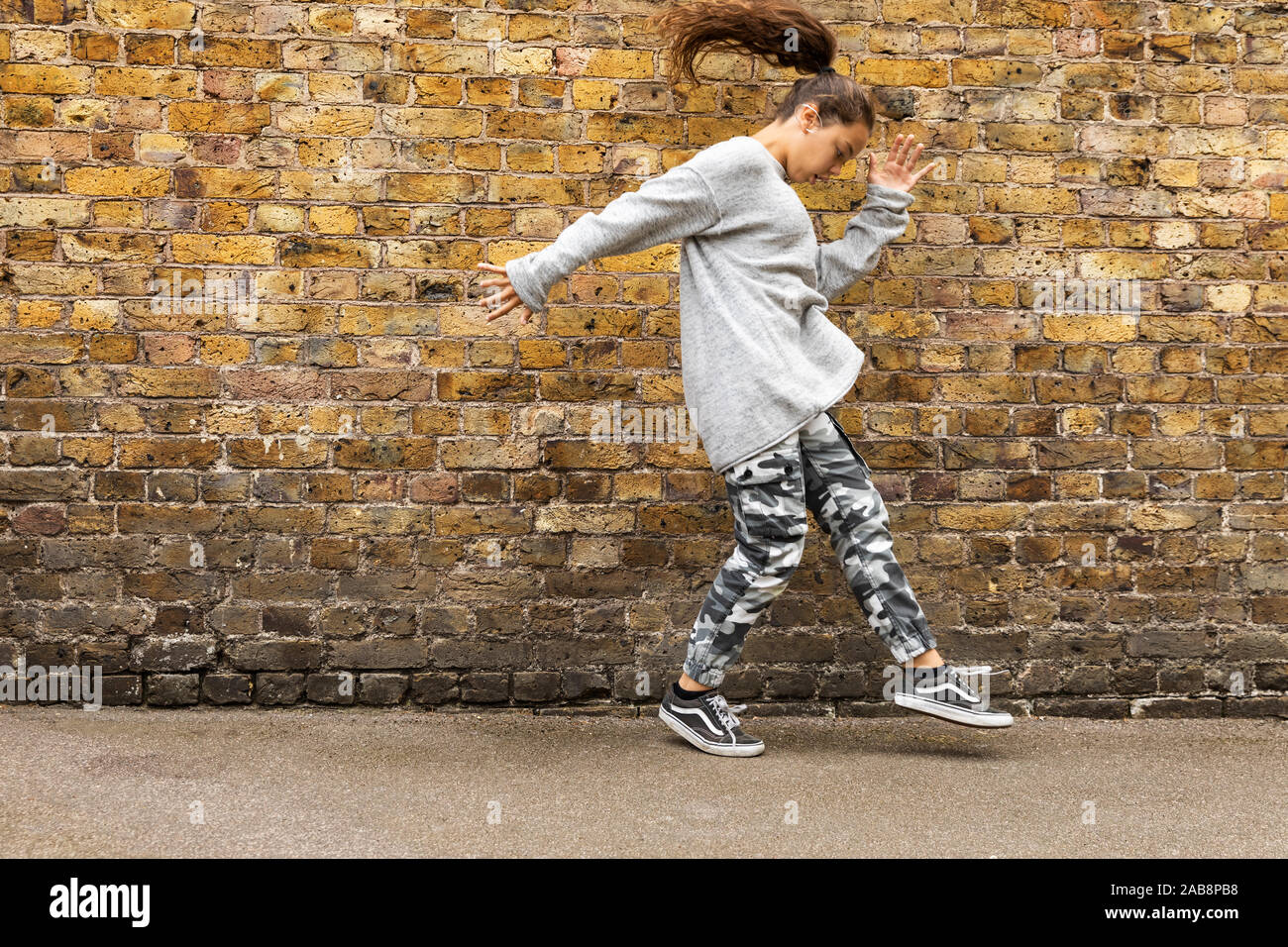 Ragazza giovane danze nella parte anteriore di un marrone un muro di mattoni. Vista frontale. Nessuno all'interno Foto Stock