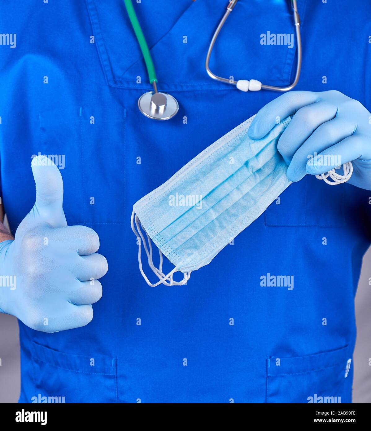 Dottore in uniforme e guanti in lattice blu mantiene maschere sterile,  l'altra parte mostra un gesto simile, uno sfondo grigio Foto stock - Alamy