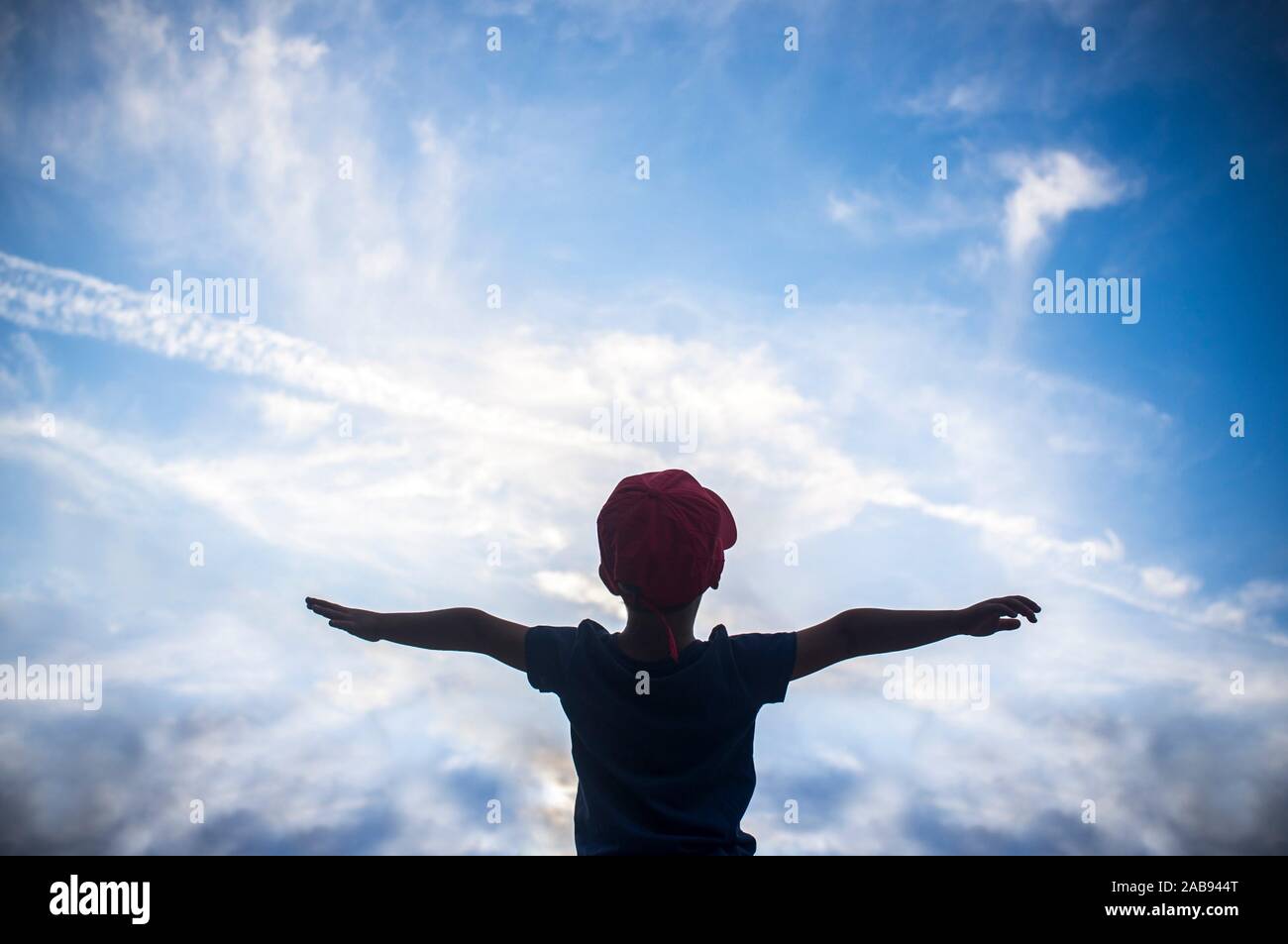 4 anni vecchio ragazzo fingendo di volare al di sopra di cielo nuvoloso. Incoraggiare i bambini fantasia concetto. Foto Stock