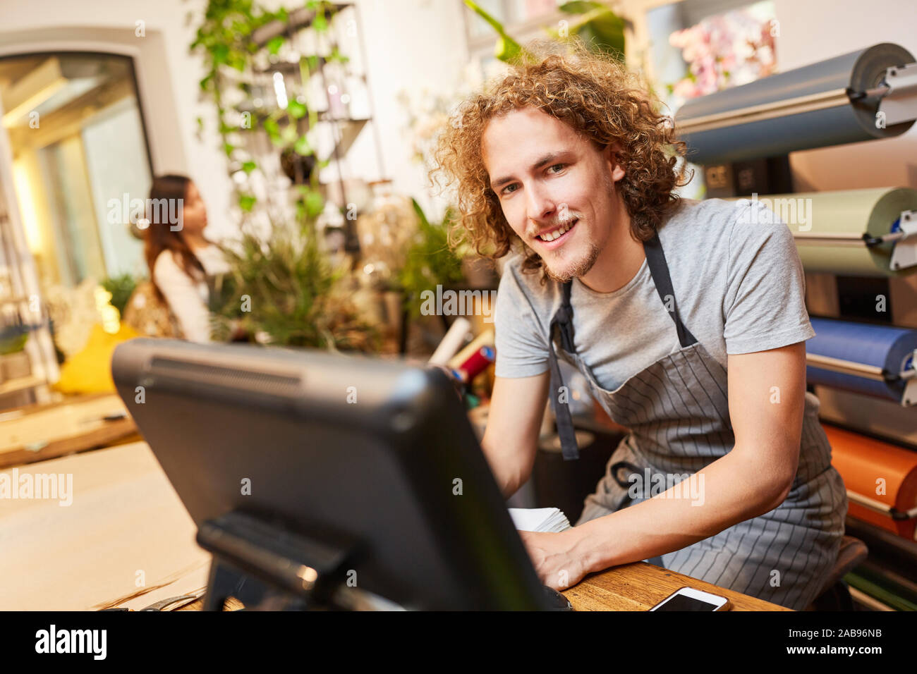 Giovane uomo come un fioraio al computer con il registratore di cassa nel negozio di fiori Foto Stock