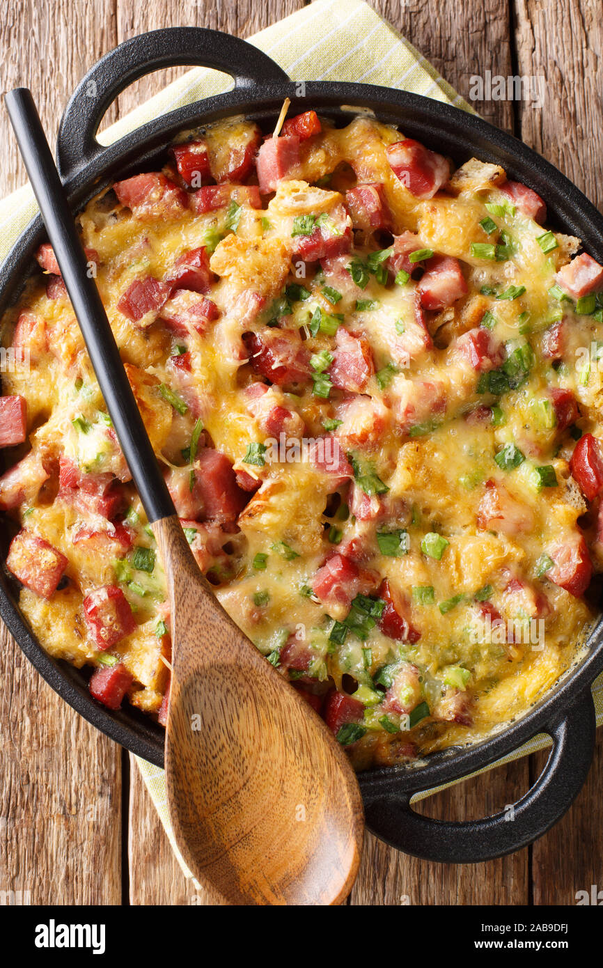 American breakfast strata con prosciutto, cipolle, formaggio e uova cotte nel forno vicino sul tavolo. Verticale in alto vista da sopra Foto Stock