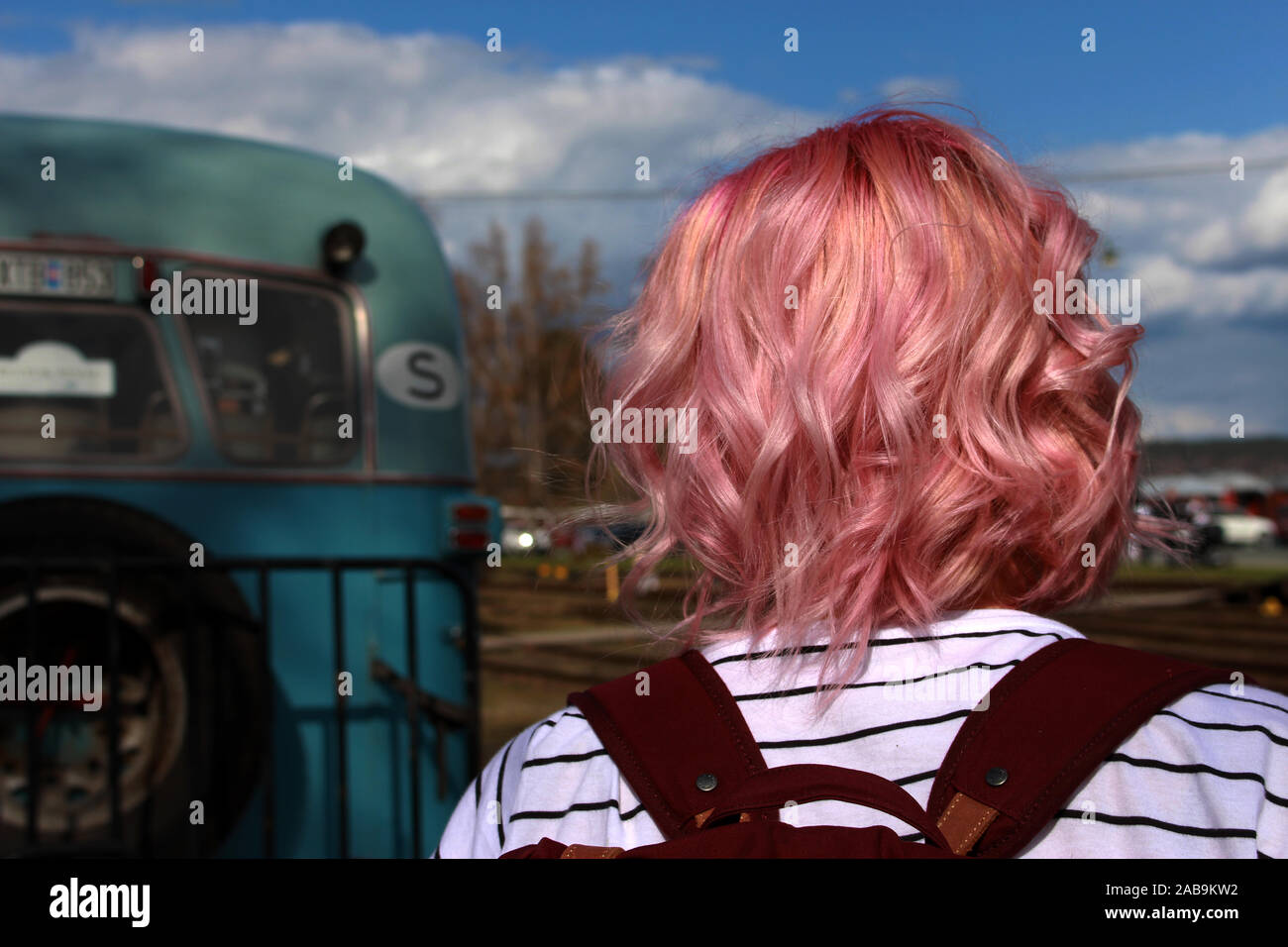 Ragazza con i capelli rosa in piedi accanto a un autobus blu Foto Stock