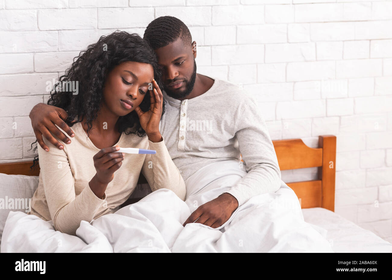Nero giovane seduto sul letto con test di gravidanza negativo risultato Foto Stock