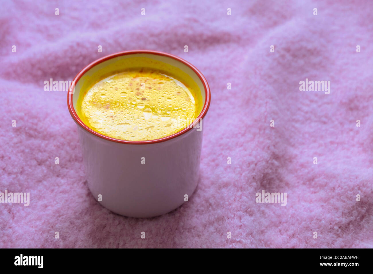 La tazza di calda bibita salutare curcuma golden latte sulla morbida maglia rosa sfondo. Foto Stock