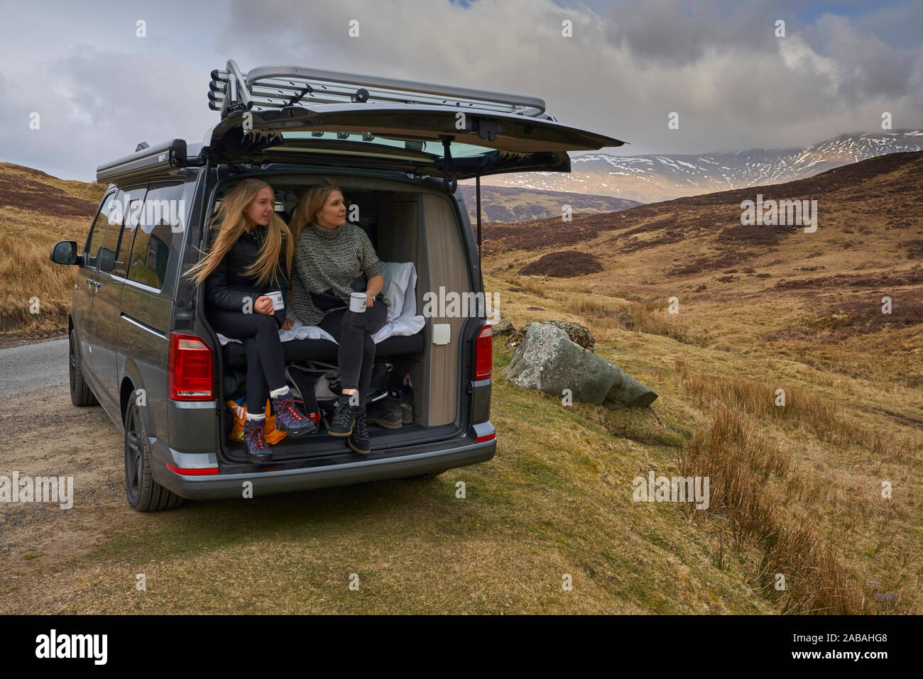 Due ragazze seduta di bere il caffè nel retro di un VW Campervan tra splendidi paesaggi nelle Highlands Scozzesi. Foto Stock