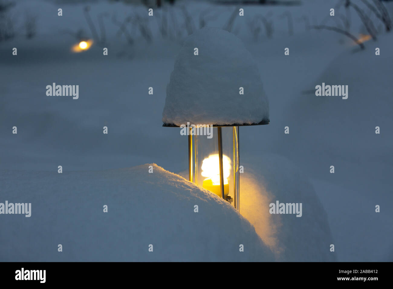 Una torcia elettrica illumina il giardino durante nevicate intense. Una lampada di strada coperta di neve crea un accogliente atmosfera festosa Foto Stock