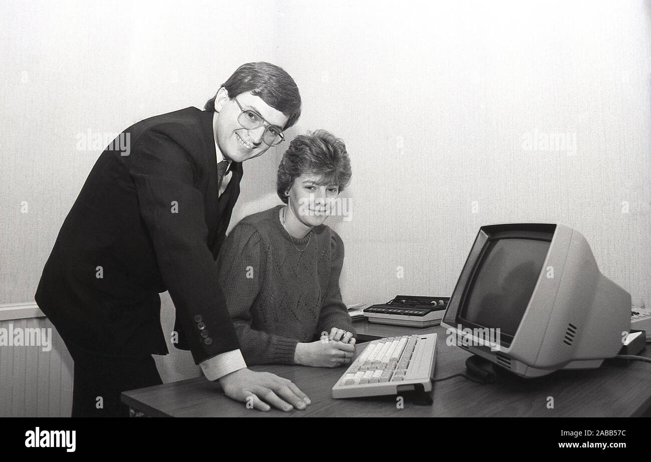 Anni '1980, un manager in costume e cravatta che posa con una giovane administratrice donna per una foto, con l'ultimo terminale e tastiera sulla sua scrivania, Inghilterra, Regno Unito. Foto Stock