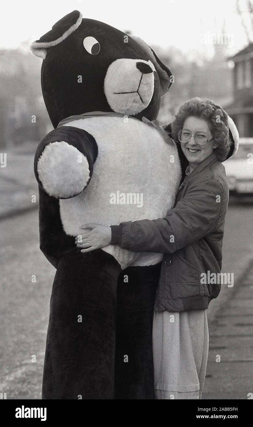 Anni '1980, una donna che abbraccia un grande giocattolo morbido, un gigantesco orsacchiotto fuori in una strada, Inghilterra, Regno Unito. Foto Stock