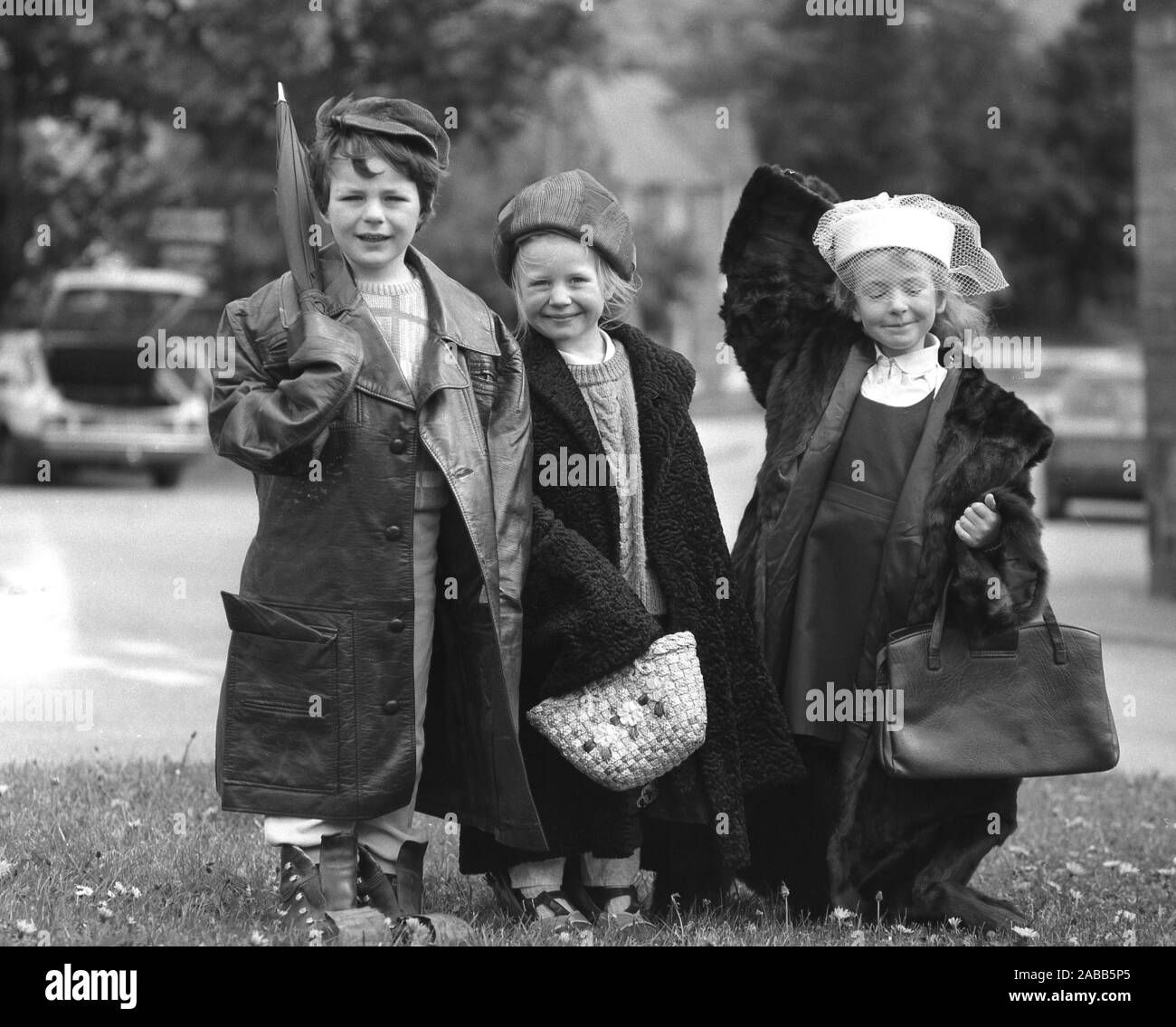 Anni ottanta, storico, tre graziose bambine vestite in alcuni della precedente generazione di adulti vestiti, cappelli e borse, che stanno per essere in vendita presso una scuola accozzaglia, compreso un 70s di moda in pelle di rivestimento e un 1940s pelliccia. Foto Stock