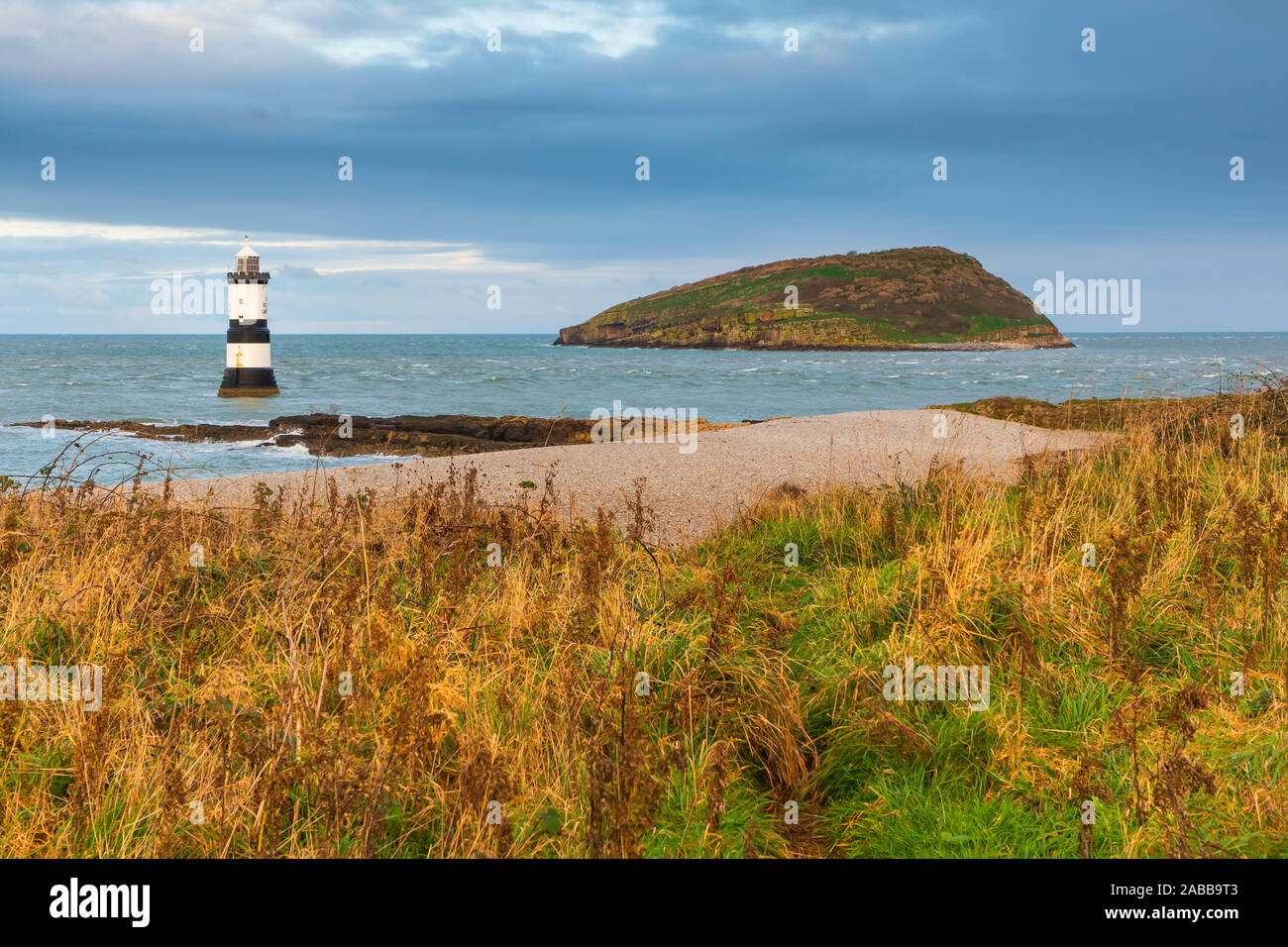 Faro Penmon (Trwyn Du Faro) sull'estremità orientale di Anglesey con Puffin Island (Ynys Seiriol) nella distanza dalla cima di una scogliera Foto Stock